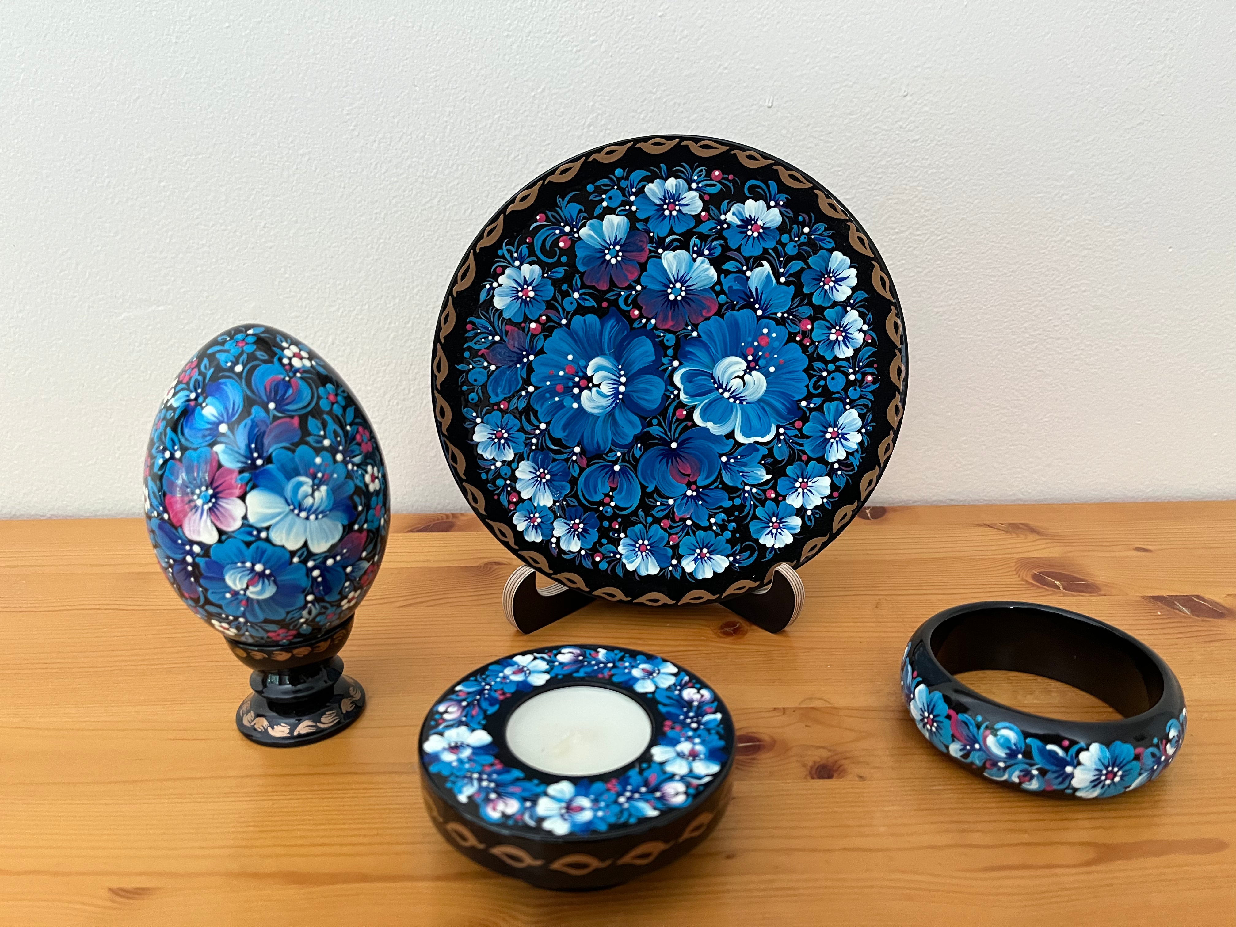 Hand-painted Blue Blossoms Petrykivka collection featuring a decorative plate, wooden pysanka, candle holder, and bracelet handmade in Ukraine